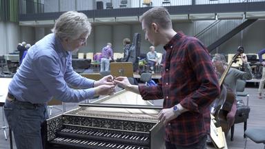 Eric Mayer steht mit einem Musiker an einem Cembalo im Probenraum der Berliner Staatsoper und lässt sich die Mechanik des Instruments erklären.