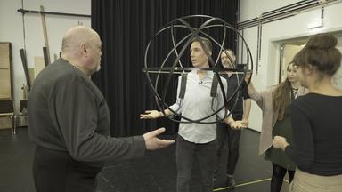 Eric Mayer trägt eine Lichtkugel auf seinem Oberkörper. Links von ihm steht der Solist Peter Rose (Pluton). Weitere Personen umgeben Eric Mayer. 