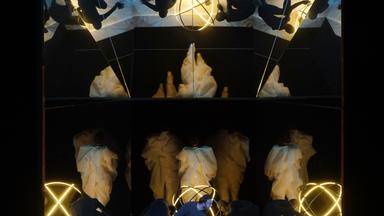  Im Vordergrund Gyula Orendt (Thésée) kniend auf Bühne. Im Hintergrund bewegen sich schwarzgekleidete Tänzer gebückt über die Bühne. Dahinter in weiße Tücher eingehüllte Tänzer.