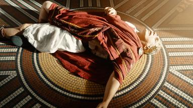 Spielszene: Der Cäsar-Darsteller liegt am Boden. Blut läuft aus seinen Mundwinkeln.