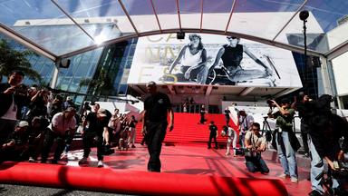 Pressefotografen und Zuschauer machen Fotos, während der rote Teppich vor dem Eingang zum Kino in Cannes ausgerollt wird.