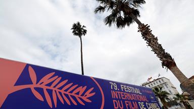 Eine Palme ragt hoch über ein lilafarbenes Plakat der Filmfestspiele von Cannes.