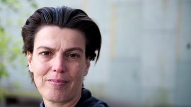 Eine Frau mit kurzem zurückgekämmtem Haar blickt in die Kamera.