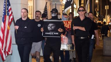 Männer in schwarzer Kleidung, teilweise vermummt, marschieren mit Fahnen und tragen das Porträtfoto eines Mannes vor sich her.