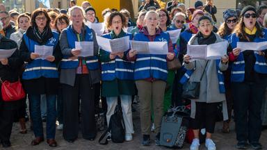 Menschen in blauen Warnwesten singen draußen