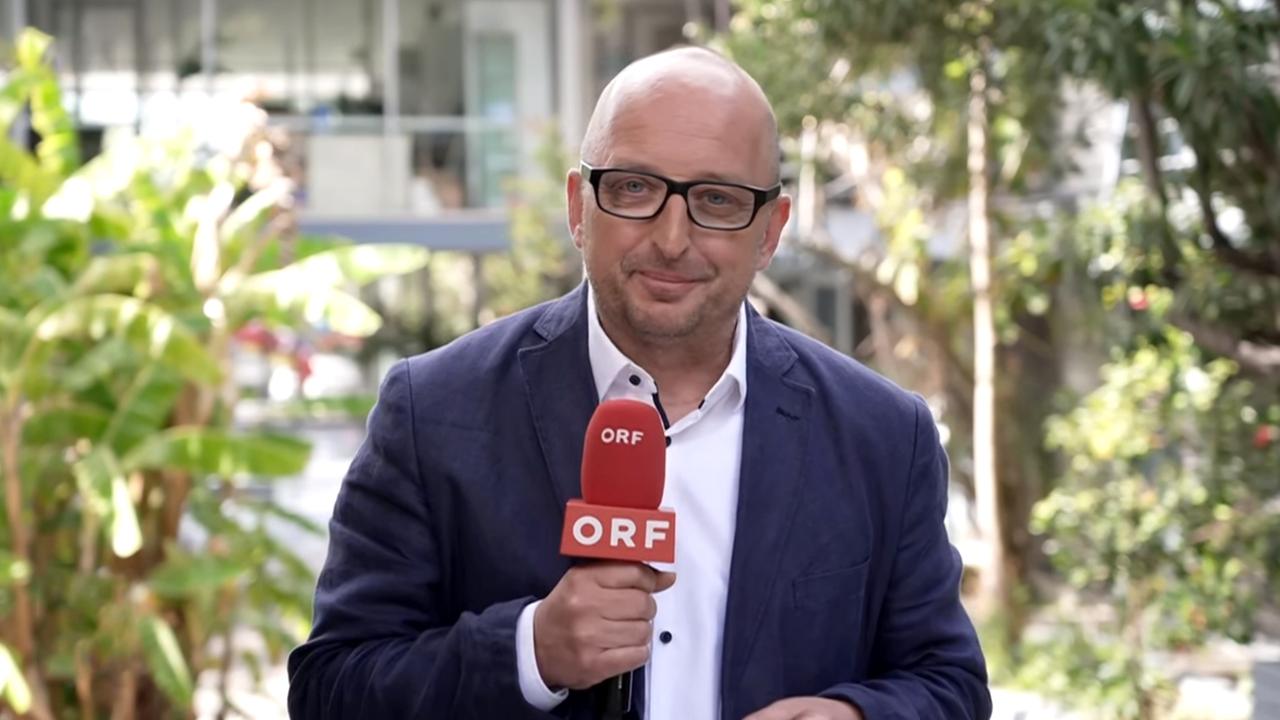 Ein Mann mit Brille und im Anzug hält ein Mikro in der Hand, auf dem ORF steht.