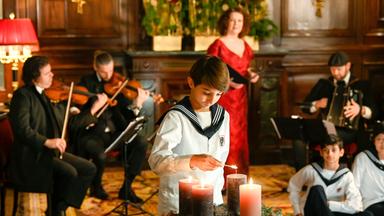 Junge zündet Kerzen am Adventskranz an, um ihn Musiker