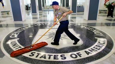 Mann putzt mit einem Schrubber über ein großes Bodenmosaik, auf dem Central Intelligence Agency United States of America steht.