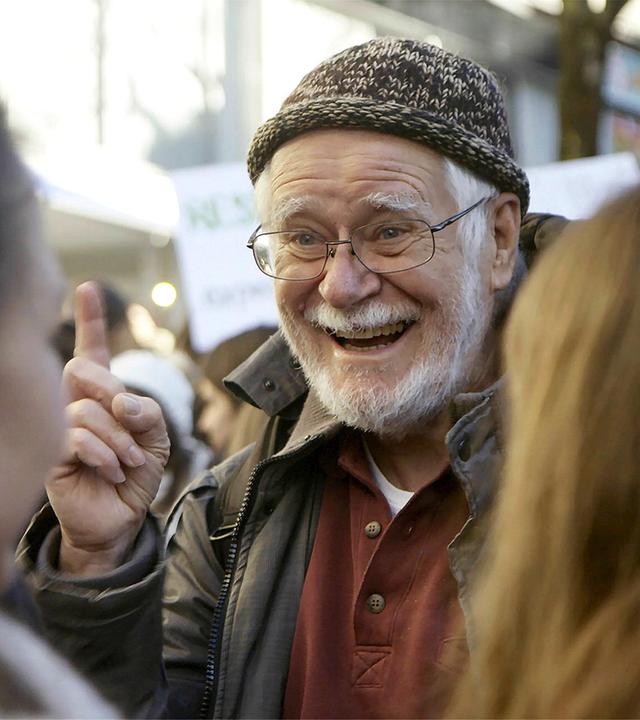 Älterer lachender Herr mit erhobenem Zeigefinger