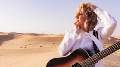 Claudia Koreck mit einer Gitarre in der Wüste.
