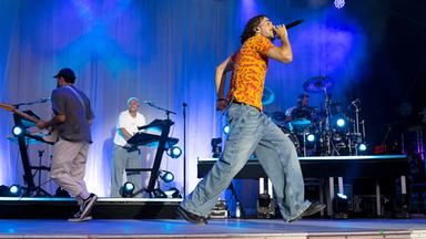 Ein junger Mann geht singend auf einer Bühne auf und ab. Hinter ihm eine Band.