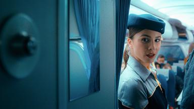 Eine Stewardess in Uniform blickt in einem Flugzeug ums Eck. 