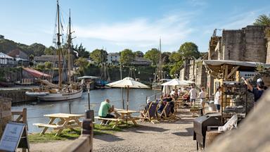 "Cornwall - Das echte Land der Rosamunde Pilcher": Der alte Hafen von Charlestown mit kleiner Promenade und einem Biergarten in der Sonne.