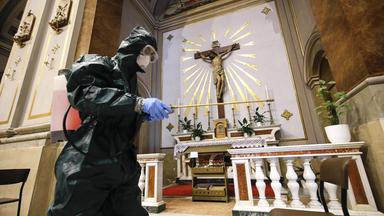 Eine Person in schwarzer Schutzkleidung desinfizert mit einem Schlauch eine Kriche.