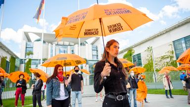 Junge Leute demonstrieren mit Regenschirmen vor dem Kanzleramt für den Generationenrettungsschirm in der Corona-Krise.