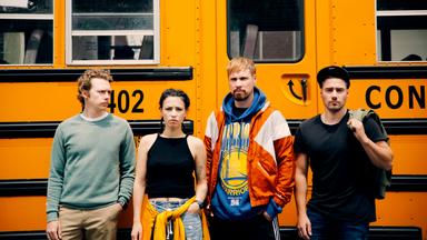 Vier junge Menschen stehen vor einem gelben Bus.