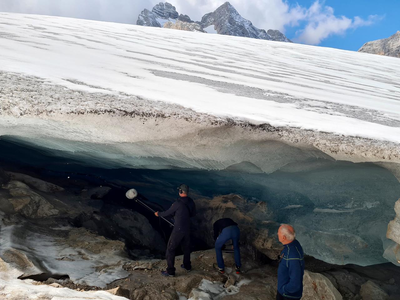 Filmcrew arbeitet am schmelzenden Dachsteingletscher, unterhalb einer mächtigen Eis- und Schneeschicht in den österreichischen Alpen.