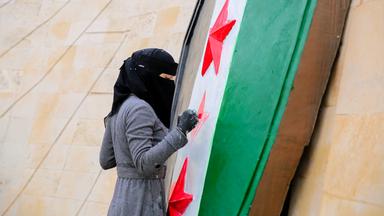 Eine Frau mit verschleiertem Gesicht mals die roten Sterne in einer schwarz weiß grün gestreiften syrischen Flagge mit frischer Farbe an.