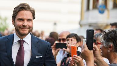 Ein junger Mann im Anzug läuft lächelnd durch eine Menschenansammlung, die ihn mit Handys fotografiert.