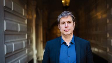 Porträtfoto eines Mannes mit leicht graumeliertem Haar in einer Toreinfahrt.