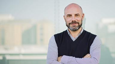 Porträtfoto eines Mannes mit Glatze und Bart, der mit verschränkten Armen in die Kamera lächelt.