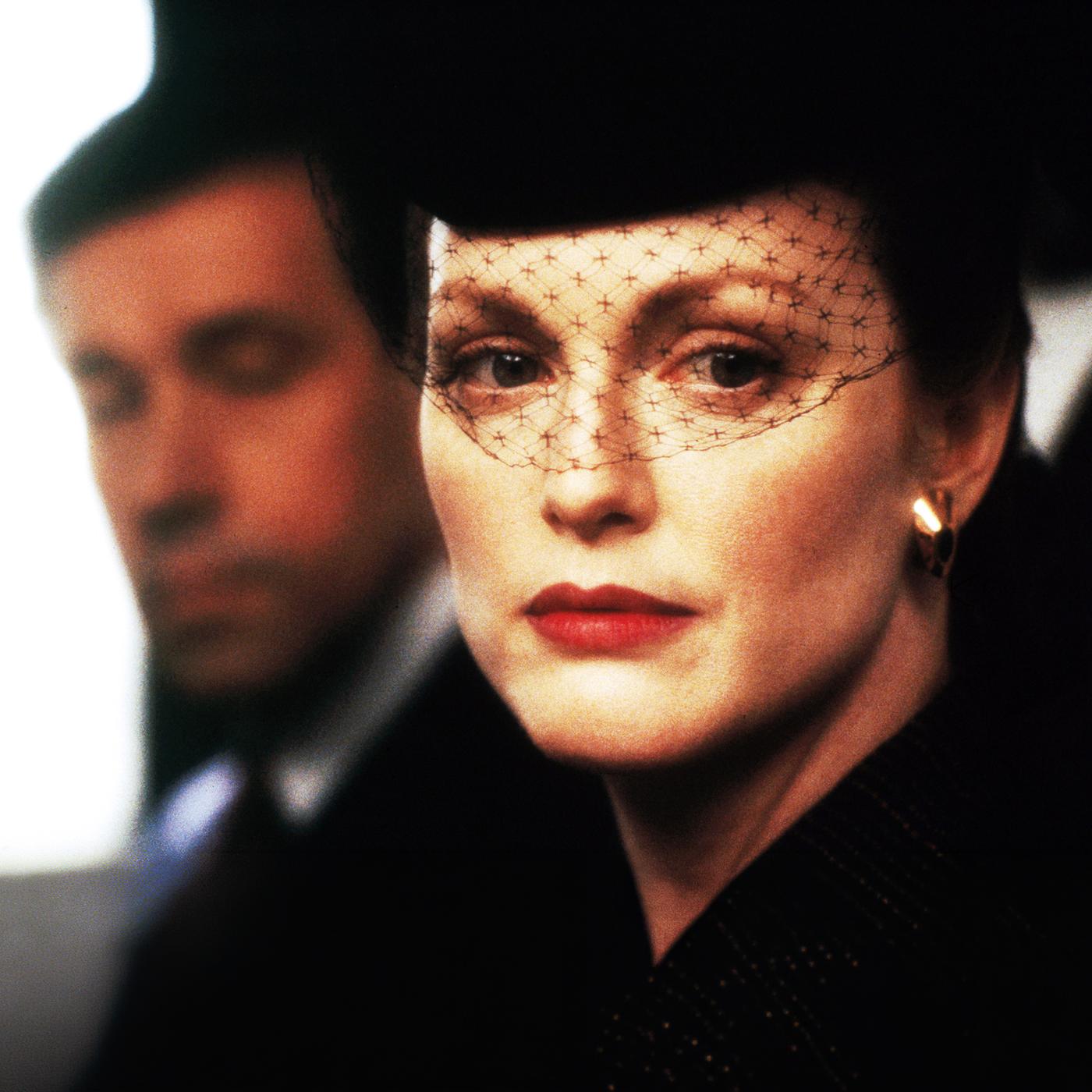 Sarah (Julianne Moore) mit einem schwarzen Gesichtsschleier aus Spitze vor ihrem Gesicht. Henry (Stephen Rea) ist etwas verschwommen im Hintergrund zu sehen.