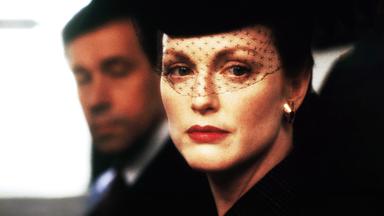 Sarah (Julianne Moore) mit einem schwarzen Gesichtsschleier aus Spitze vor ihrem Gesicht. Henry (Stephen Rea) ist etwas verschwommen im Hintergrund zu sehen.