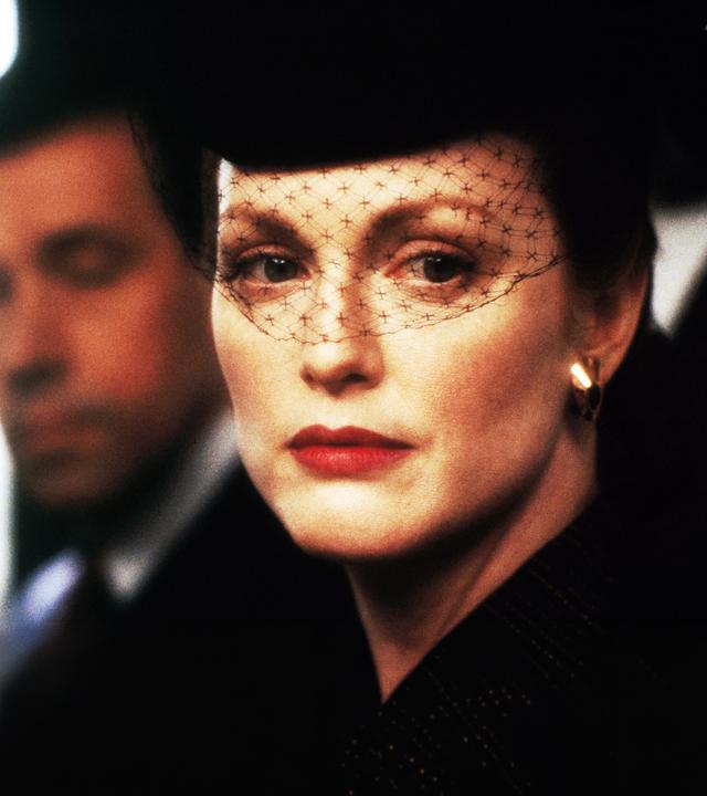 Sarah (Julianne Moore) mit einem schwarzen Gesichtsschleier aus Spitze vor ihrem Gesicht. Henry (Stephen Rea) ist etwas verschwommen im Hintergrund zu sehen.