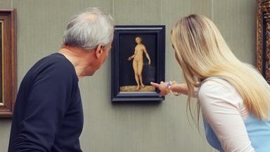 Ein älterer Mann und eine Frau betrachten ein Gemälde von Lucas Cranach, das Adam und Eva zeigt, in einer Gemäldegalerie.