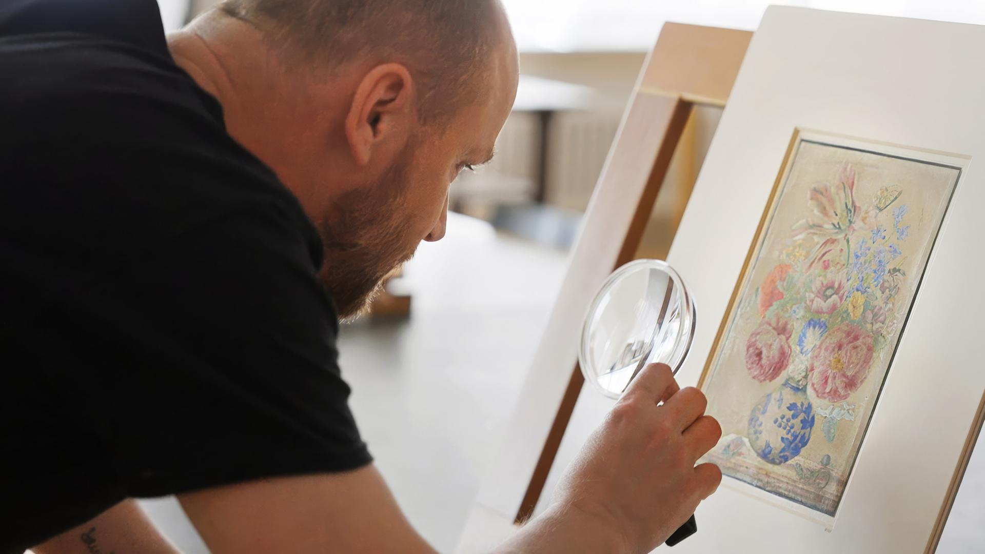 Ein Mann untersucht mit einer Lupe ein botanisches Aquarell mit Blumen von Maria Sibylla Merian.