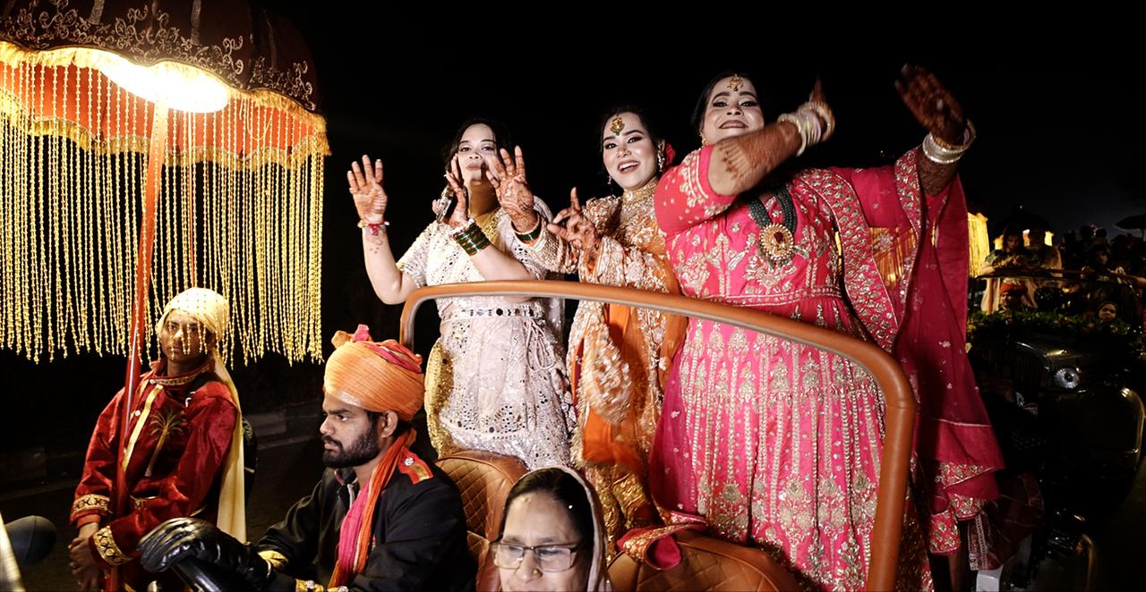 Drei Frauen stehen auf einem Gefährt. Sie tragen Schmuck und schöne Kleider.