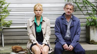 Eine Frau sitz neben einem Mann, beide blicken ernst nach vorn.