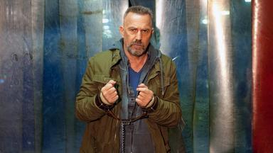 Gefesselter Mann blickt böse in die Kamera.