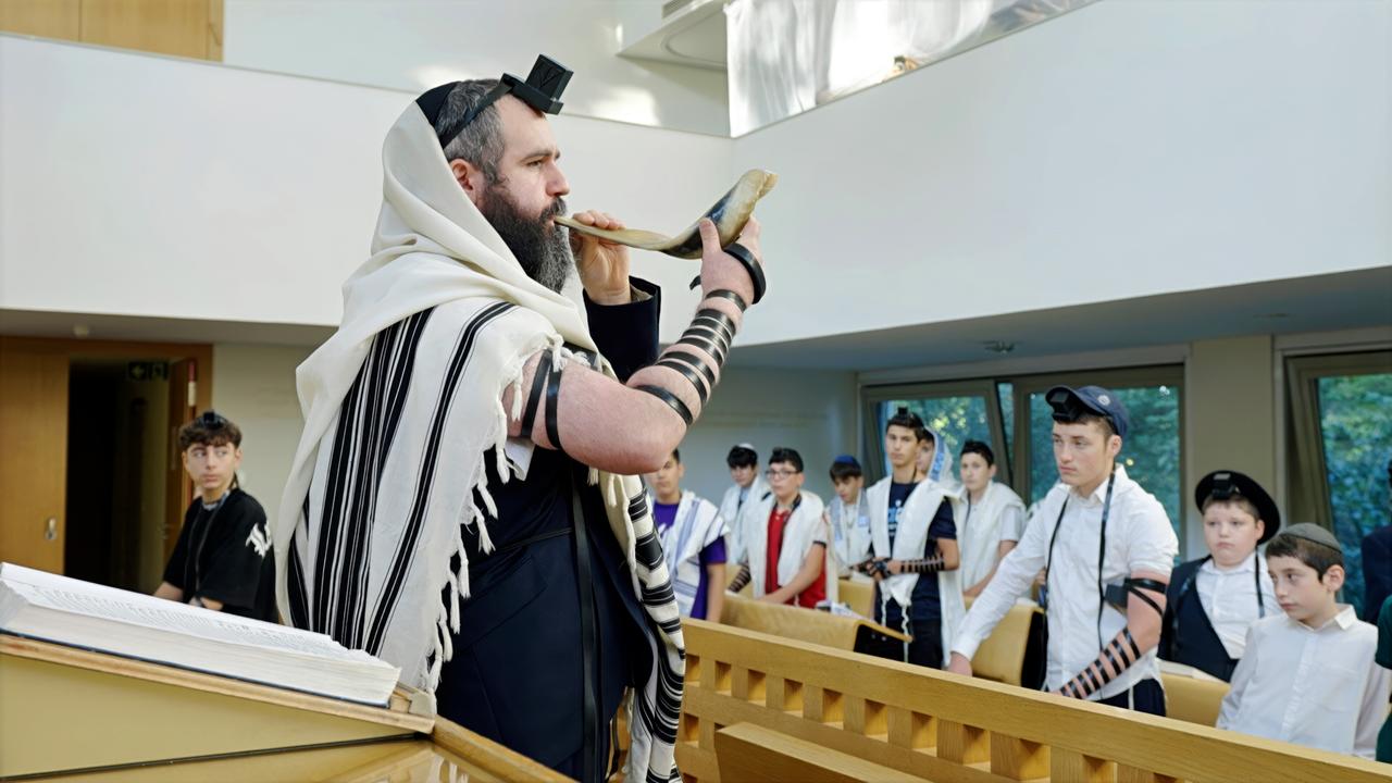 Viele Jungen schauen auf einen Mann in traditioneller jüdischer Kleidung, der in ein Instrument bläst