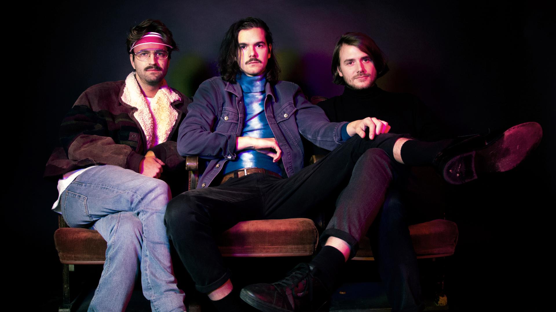 Drei junge Männer sitzen auf einem Sofa.