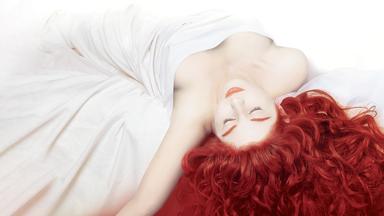 Ein junge, nackt scheinende Frau liegt unter einer großen weißen Decke. Ihre Haut ist bleich, ihre ausgebreiteten langen, lockigen Haare sowie Lippen und Augenbrauen sind leuchtend rot. Der Kopf liegt zum Betrachter hin leicht nach unten hängend, ihr linker, nach hinten ausgestreckter Arm fällt ebenfalls leicht nach unten weg.