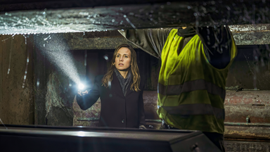 Frau steht ausgerüstet mit einer Taschenlampe und einem Kollegen in einer Gruft.