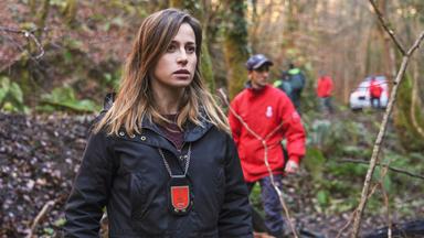 Kommissarin steht in einem Wald und schaut bestürzt.