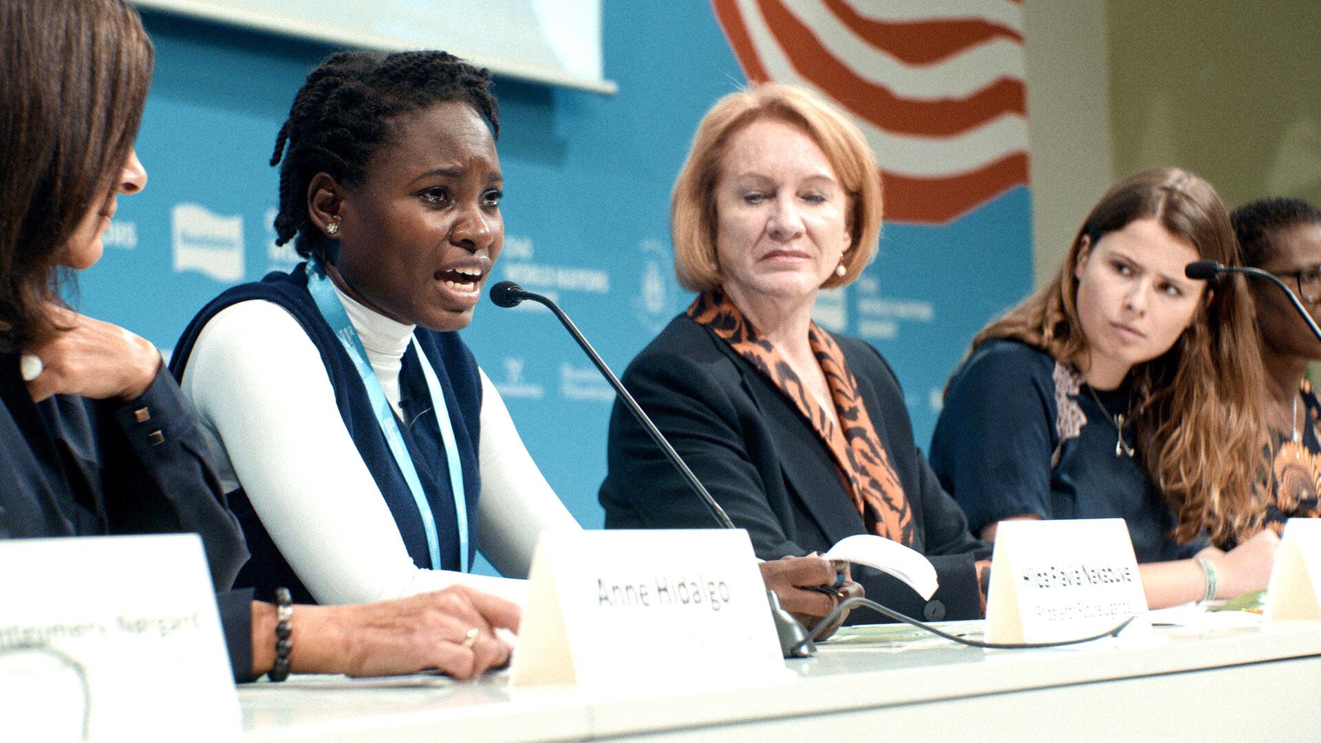 Junge Frau aus Uganda bei einer Podiumsdiskussion mit weiteren Teilnehmern