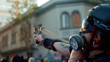 Tätowierter junger Mann mit Helm und Gasmaske schießt mit Steinschleuder