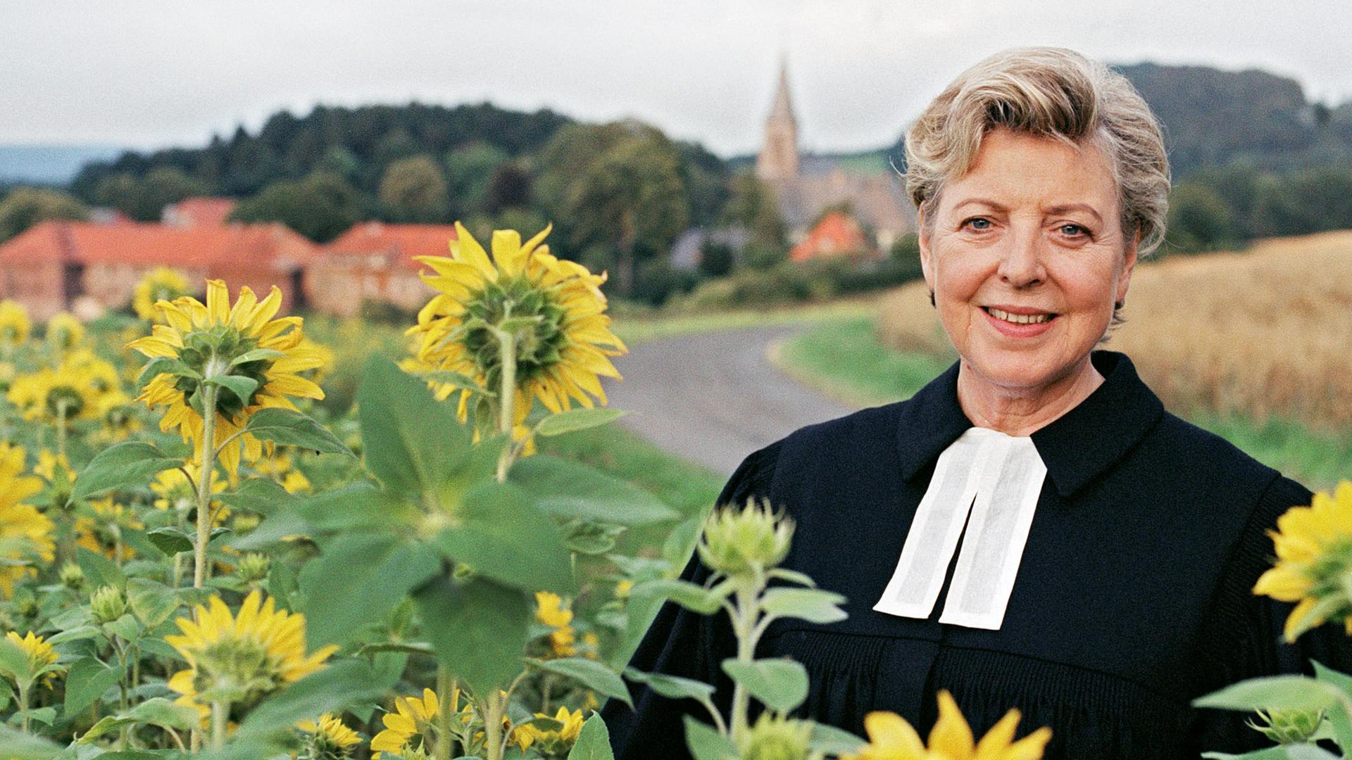 Eine Frau in Talar auf einem Sonnenblumenfeld.
