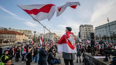 Auf einem großen Platz in einer Großstadt haben sich zahlreiche Menschen mit weiß-rot gestreiften Flaggen versammelt.