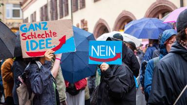 Bei einer Demonstration halten Menschen, die unter Regenschirmen nicht zu erkennen sind, Plakate gegen die AFD.