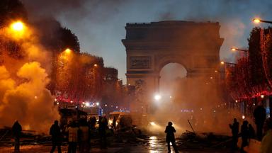 Demonstration vor dem Triumphbogen in Paris, orangener Rauch, Schattengestalten auf der Straße. Abends/Nacht.