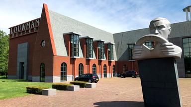 Ein großes Gebäude mit der Statue eines Mannes mit Lenkrad im Vordergrund. 