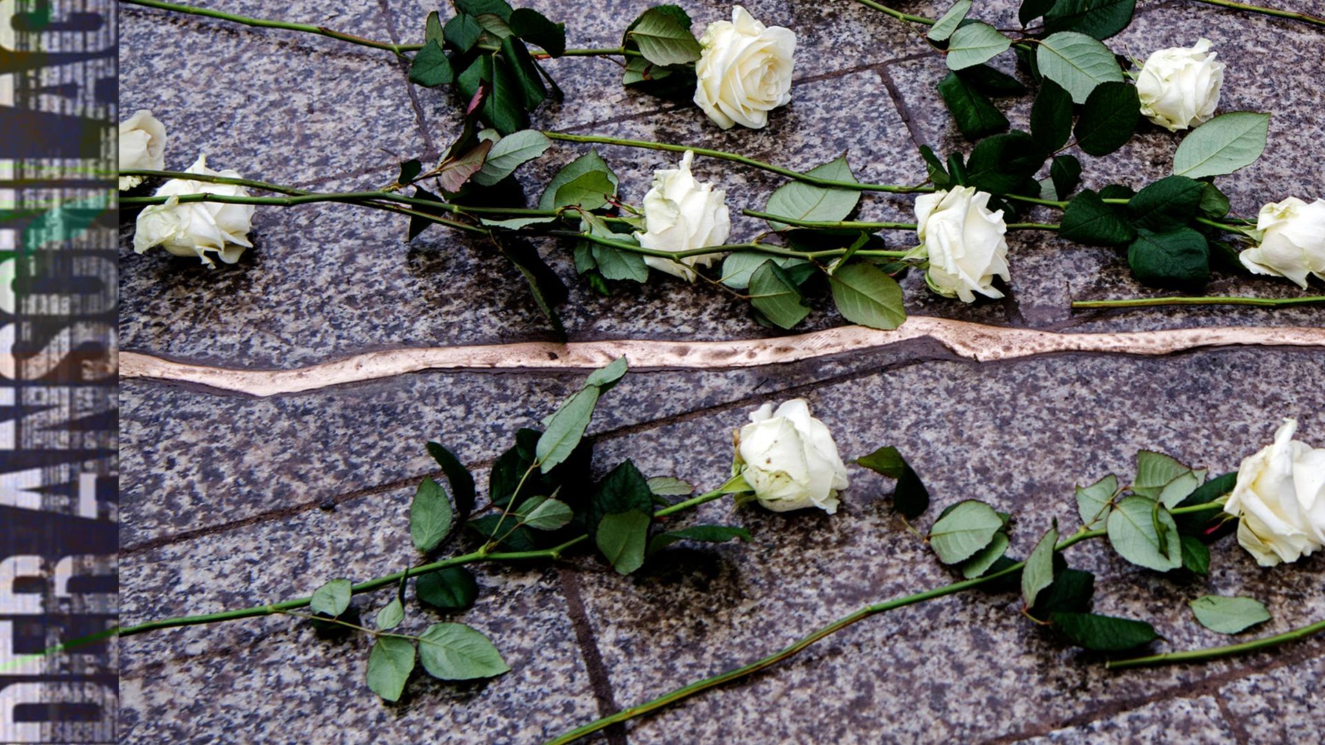 Ein mit Metall ausgegossener Riss im boden des berliner breitscheidplatzes erinnert an die opfer des terroranschlags 2016, darauf liegen weiße Rosen