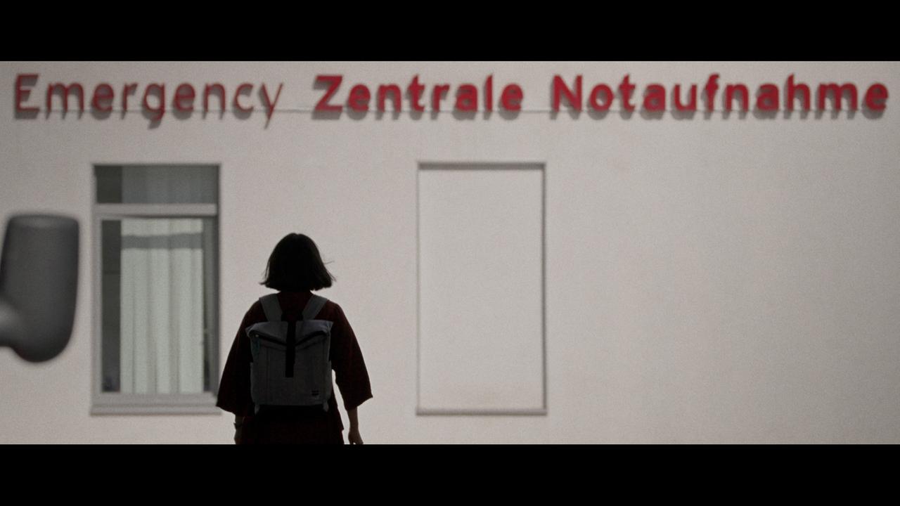 Frau von hinten vor Krankenhaus mit Aufschrift "Emergency".