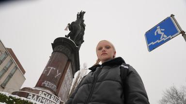 Eine junge Frau vor einer Reiterstatue, die mit Graffiti beschmiert ist.