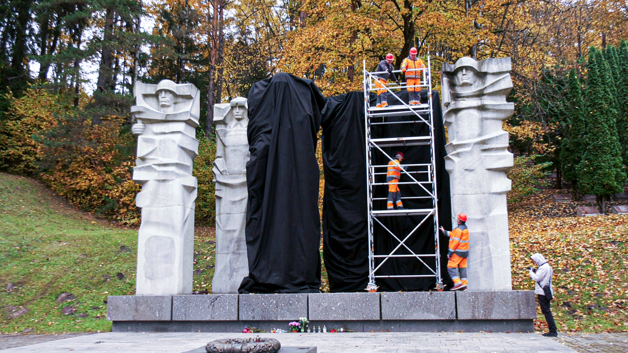 Männer verhüllen 5 große Statuen mit schwarzen Tüchern