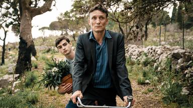 Ein Mann auf einem Fahrrad. Auf dem Gepäckträger sitzt ein Junge.